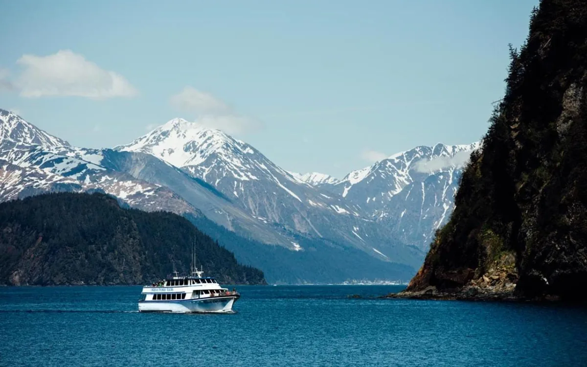 A tour boat under snow-covered cliffs in Kenai Fjords National Park, Alaska
